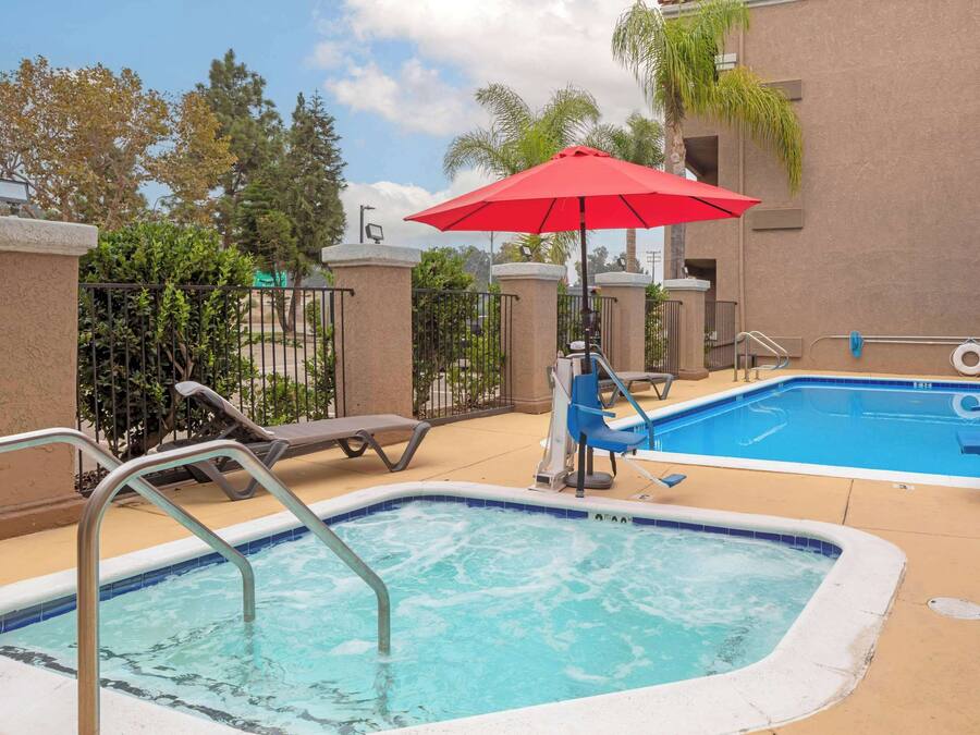 A pool area with a hot tub, lounge chairs, and a red umbrella.