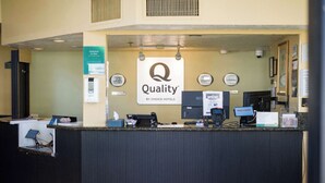 Un comptoir d’accueil d’hôtel avec une pancarte indiquant « Qualité », une horloge numérique et une pancarte « Bienvenue ».