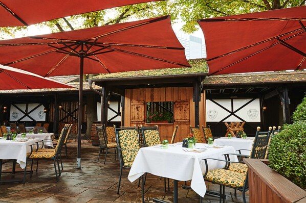 An outdoor dining area with tables and chairs, red umbrellas, and wooden paneling.