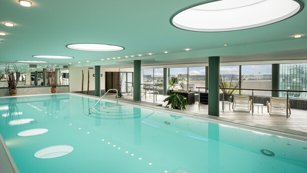 A spacious indoor swimming pool with a clear view of the city skyline through large windows.