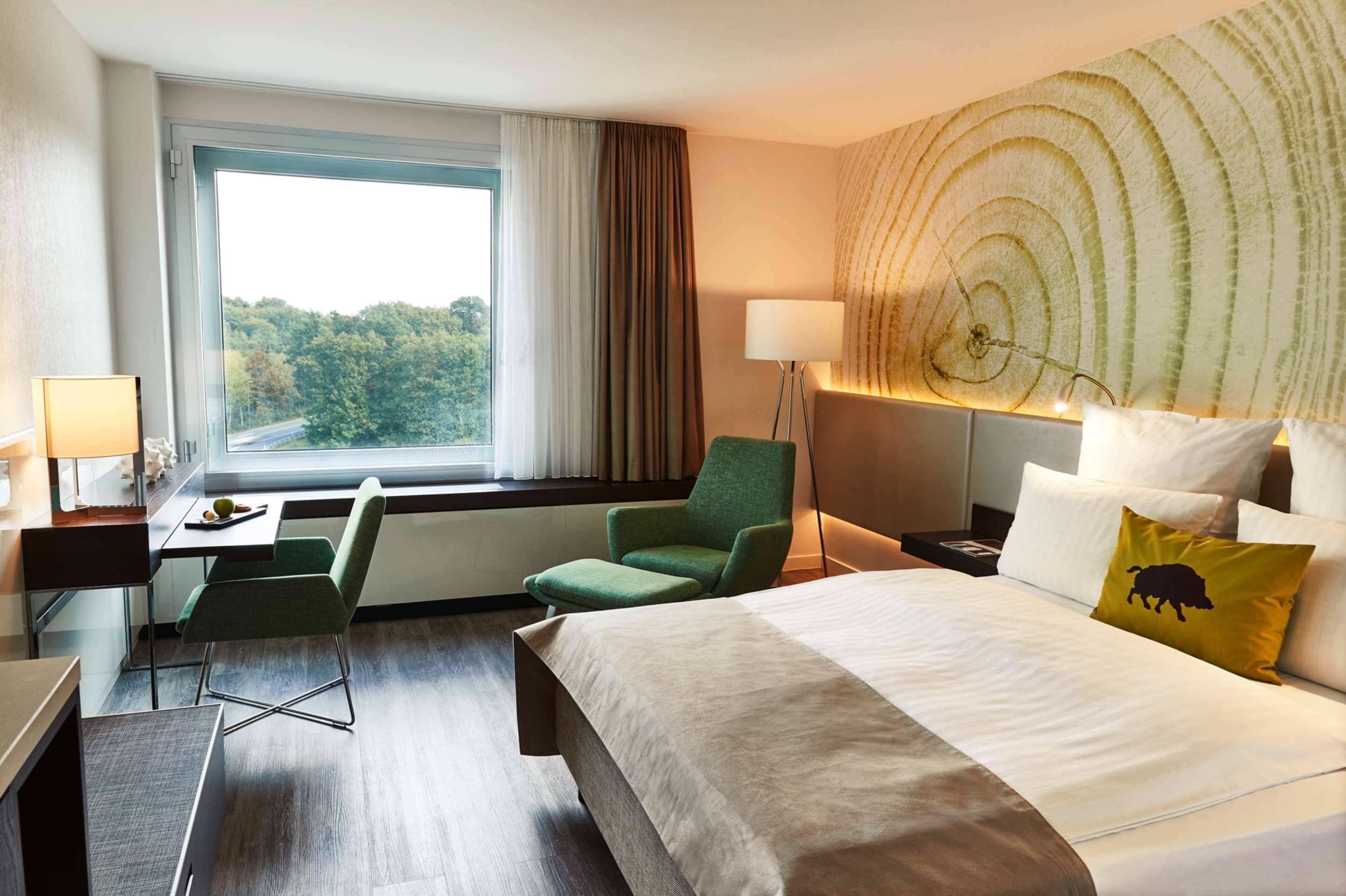 Habitación de hotel con cama, escritorio, silla, lámpara y vistas al exterior.