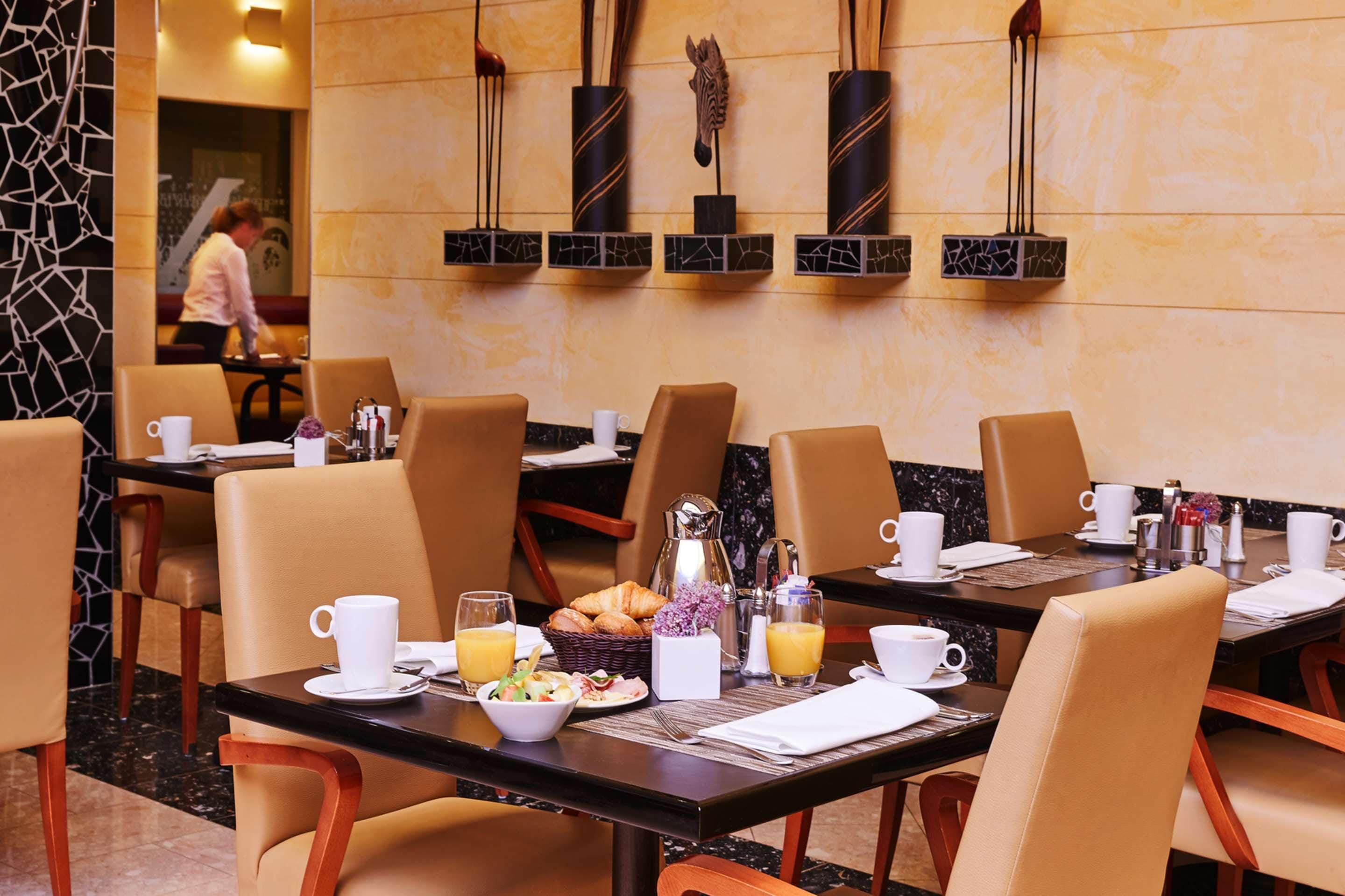 Un comedor de hotel con mesas preparadas para el desayuno, incluyendo cruasanes, fruta y café.