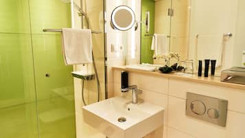 Un baño moderno con un lavamanos blanco, cabina de ducha con mampara de vidrio y pared revestida de azulejos verdes.