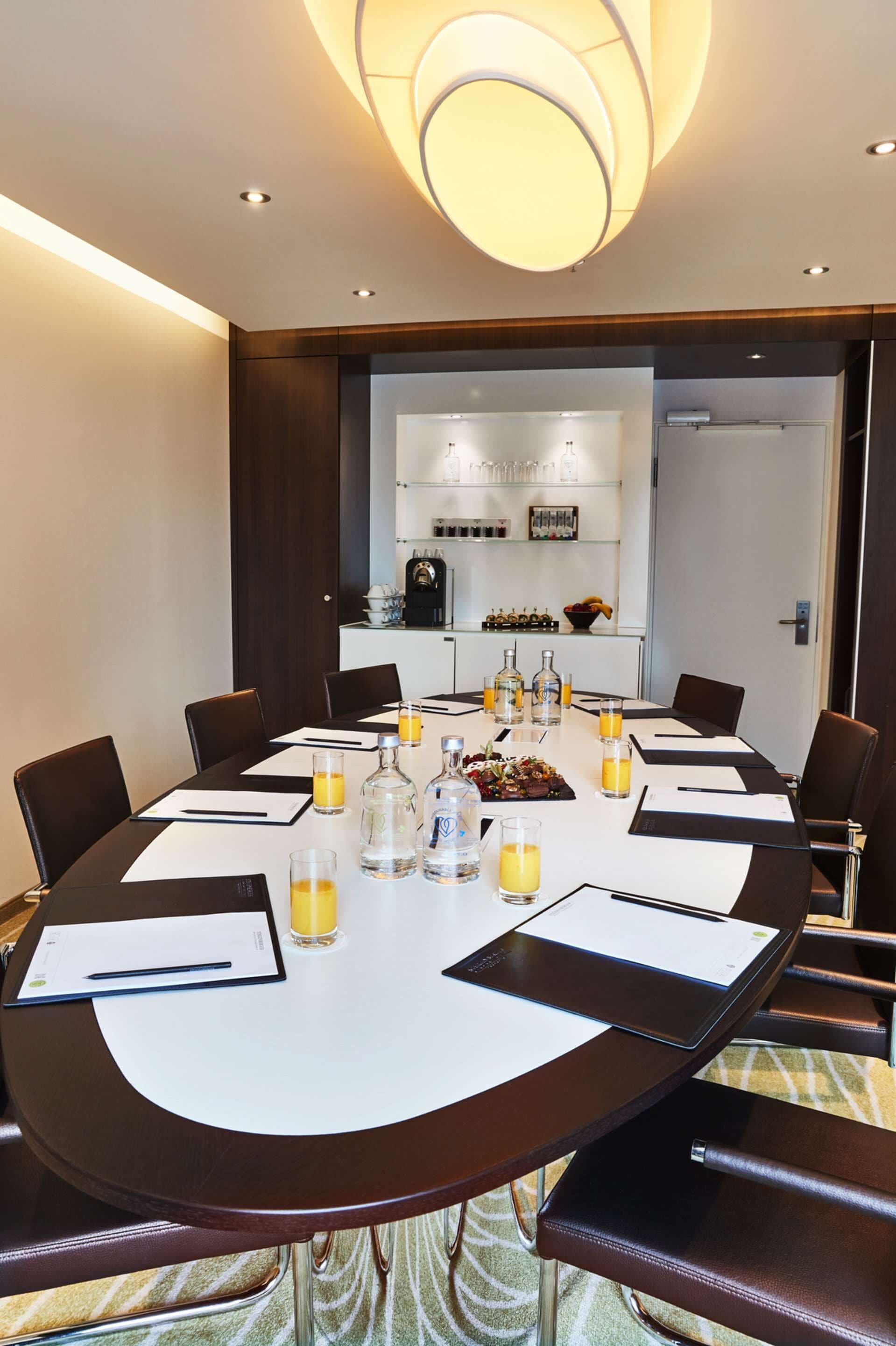 A conference room with a round table, chairs, and a central light fixture.