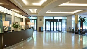 A modern hotel lobby with a reception desk, seating area, and large glass doors leading outside.