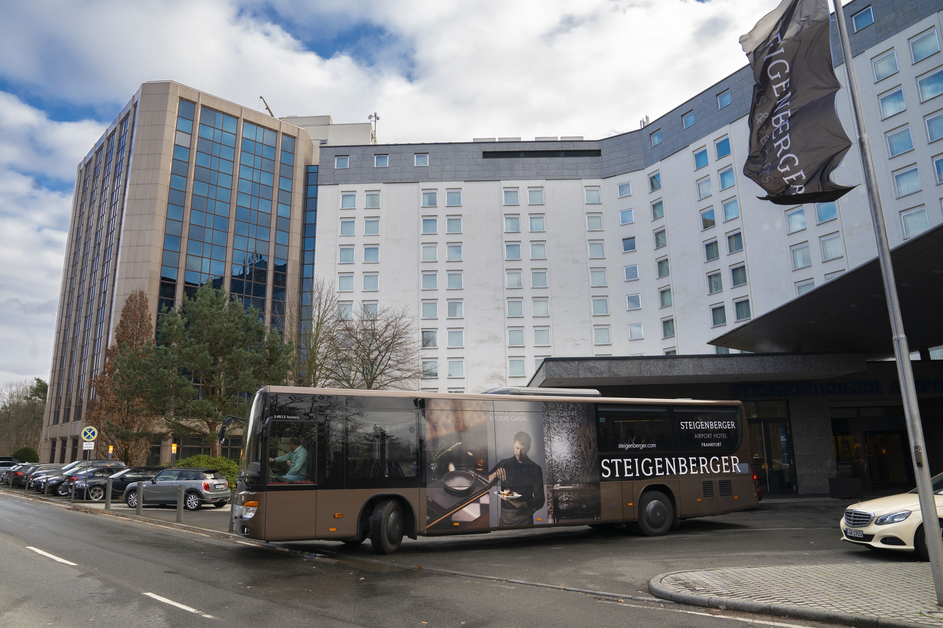 A bus with an advertisement for Steigenberger Airport Hotel parked in front of a hotel building.