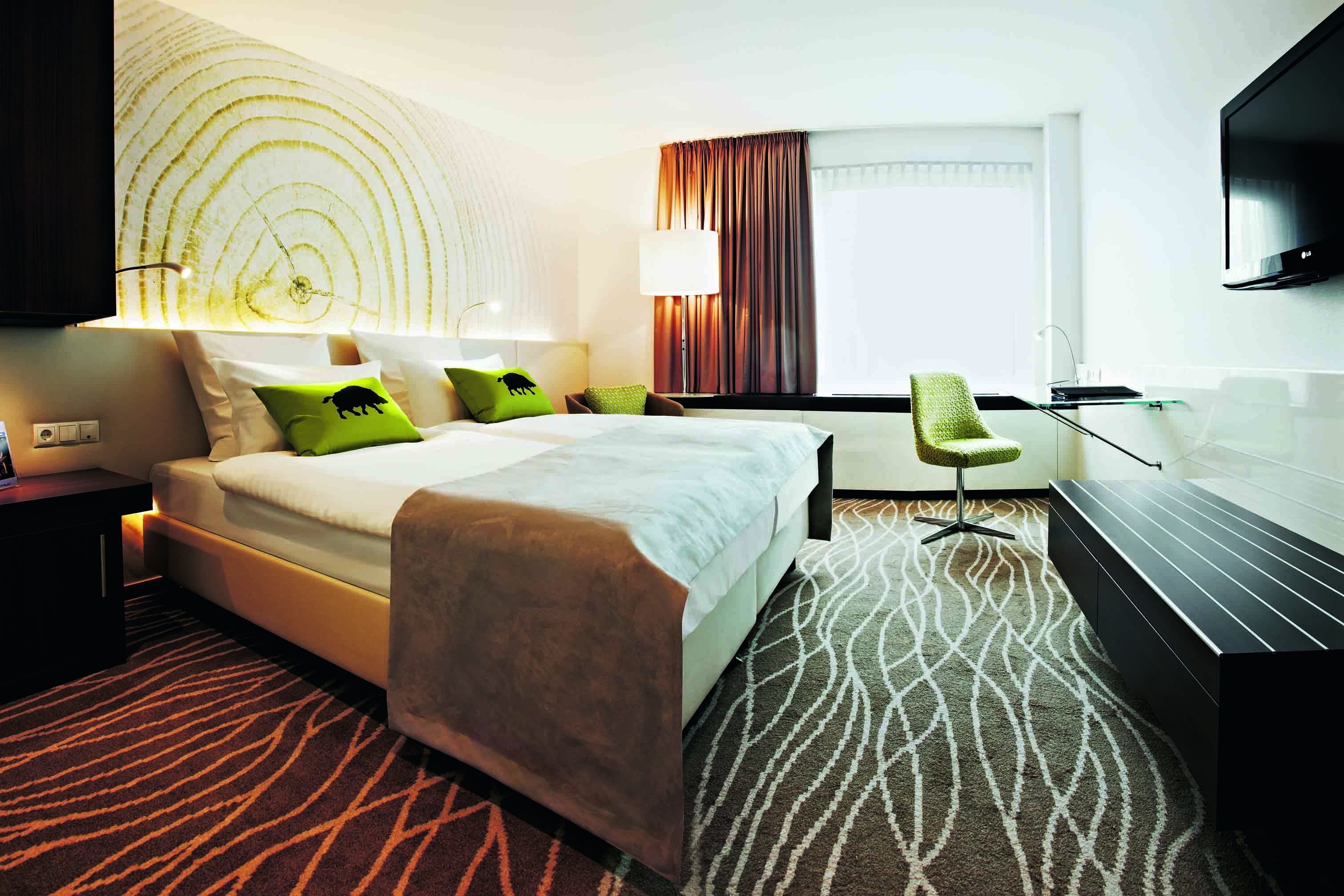 A hotel room with a large bed, a desk, a chair, a TV, and a patterned carpet.