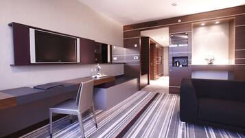A modern hotel room with a flat-screen TV, a desk with a chair, a sofa, and a striped carpet.