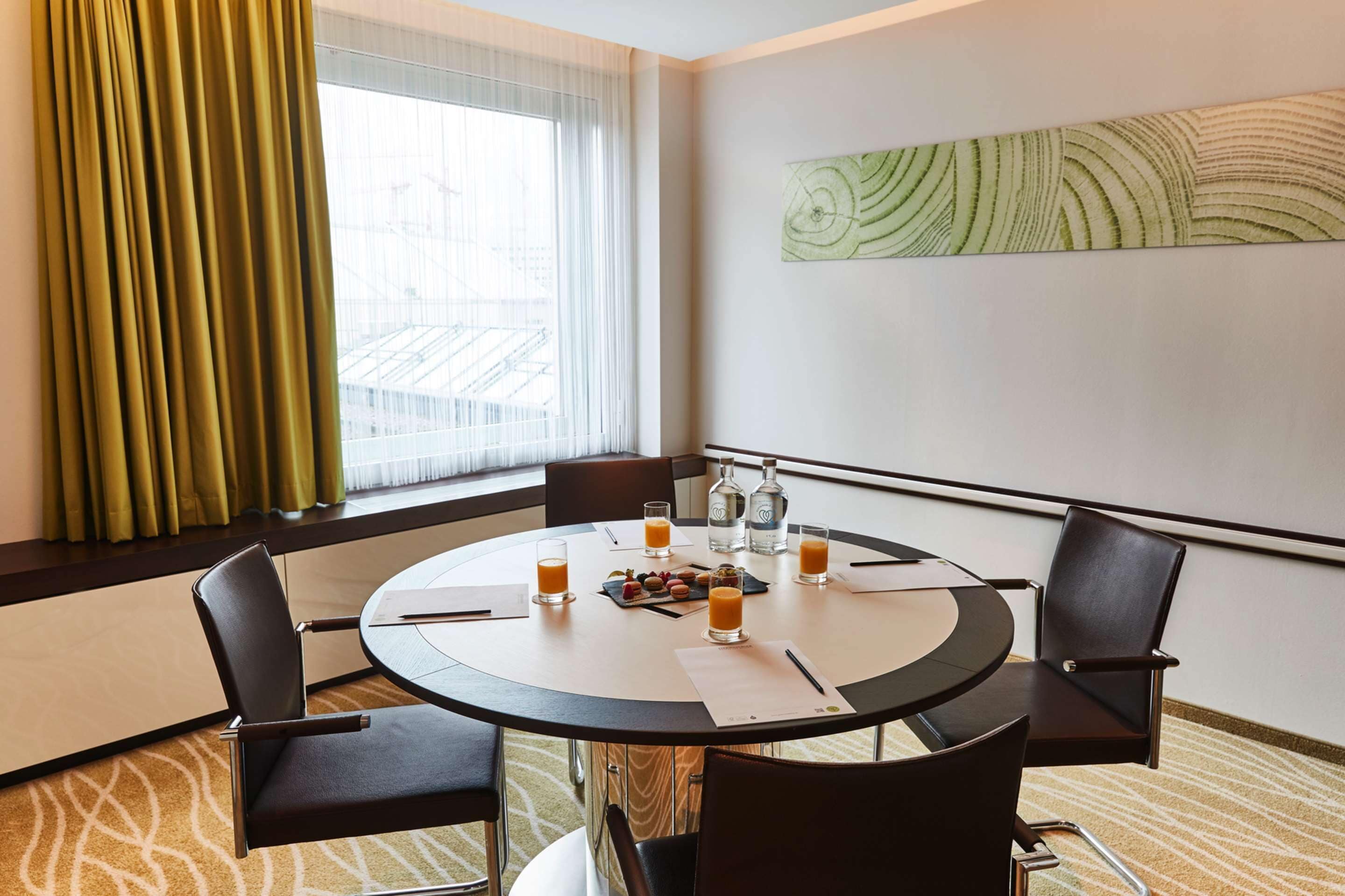 A conference room with a round table, four chairs, a bottle of water, glasses of orange juice, and a fruit plate.