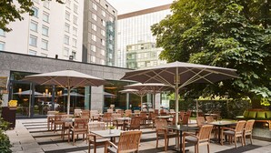 An outdoor seating area with tables and chairs, large umbrellas, and a view of a modern building.