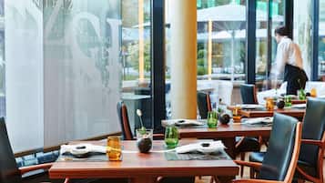 Un restaurante con mesas y sillas de madera, copas de vidrio transparente y vistas al exterior.