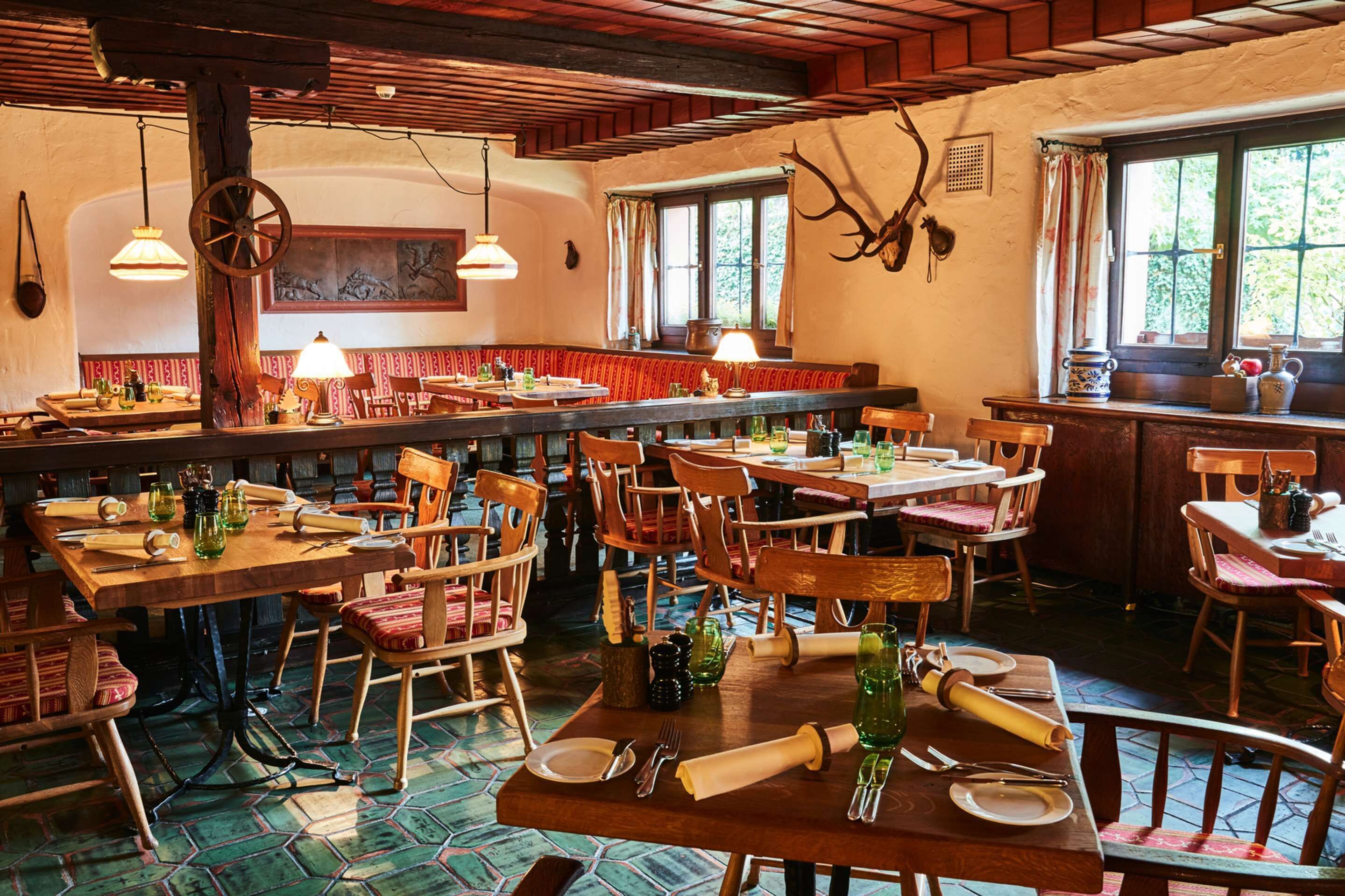 Un comedor rústico con mesas y sillas de madera, techo con vigas de madera y una ventana con cortinas.
