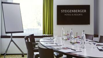 Uma sala de conferências com um quadro branco, uma mesa posta para reuniões e um aviso para Steigenberger Hotels & Resorts.
