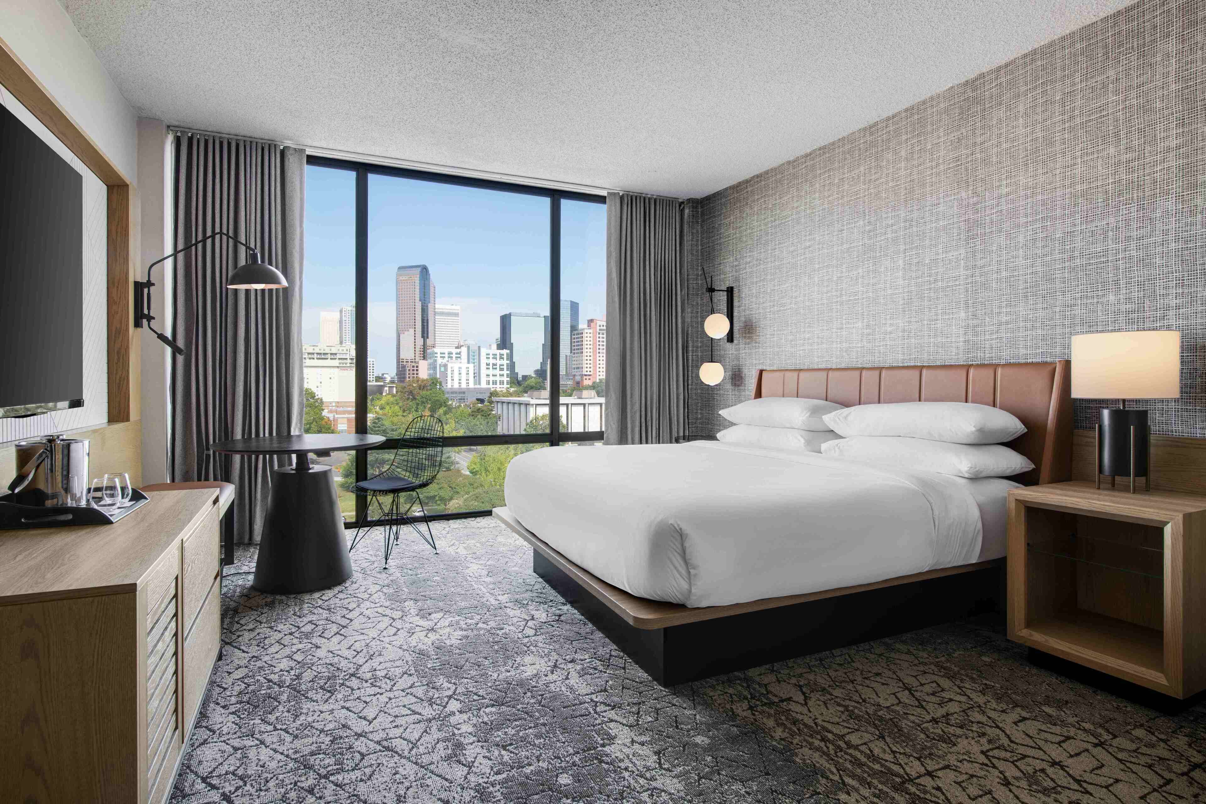 A modern hotel room with a large bed, a desk, and a view of the city skyline.
