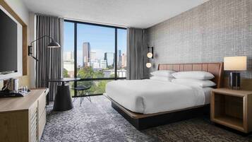 A modern hotel room with a large bed, a desk, and a view of the city skyline.