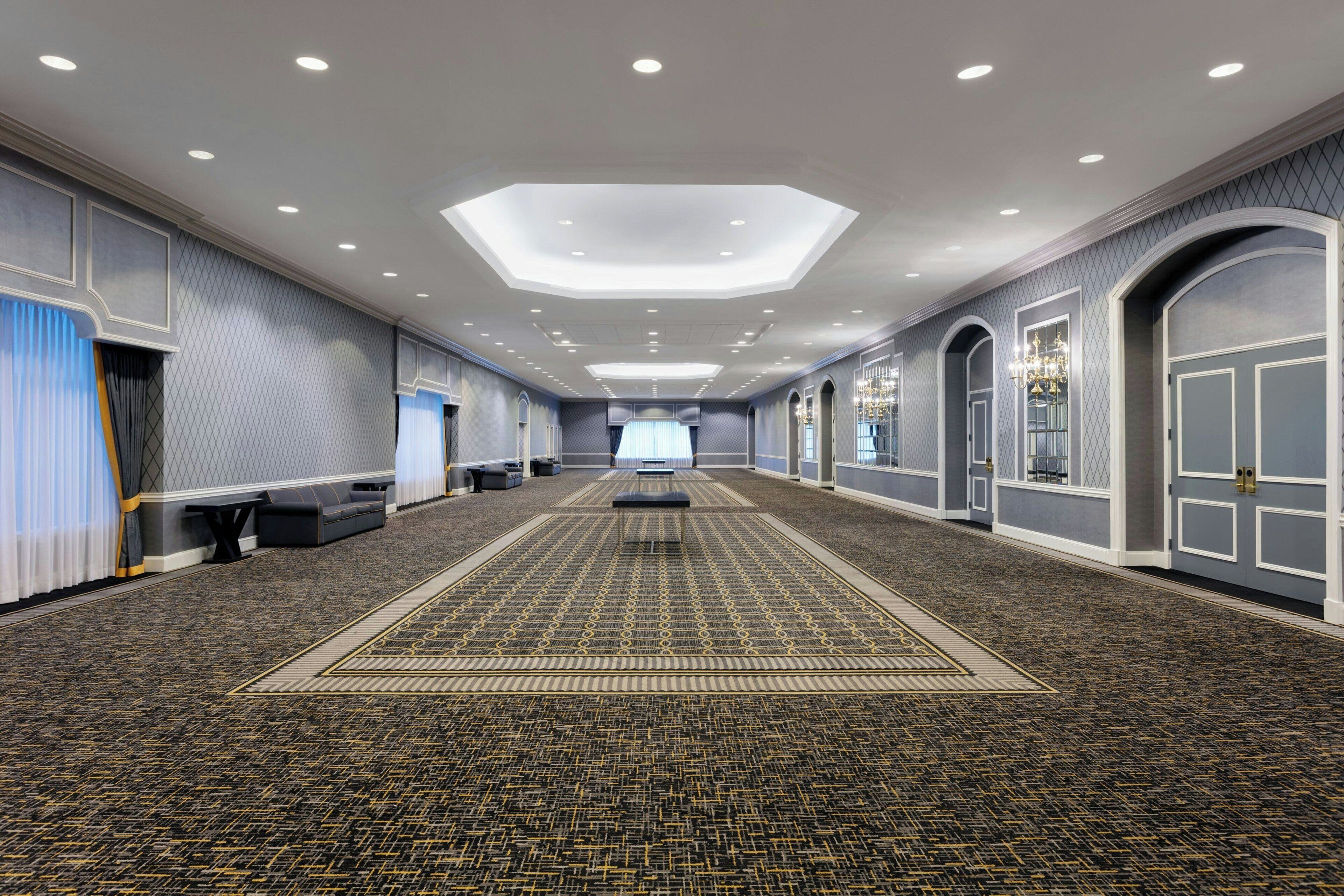 A spacious hotel corridor with a patterned carpet, recessed lighting, and arched doorways.