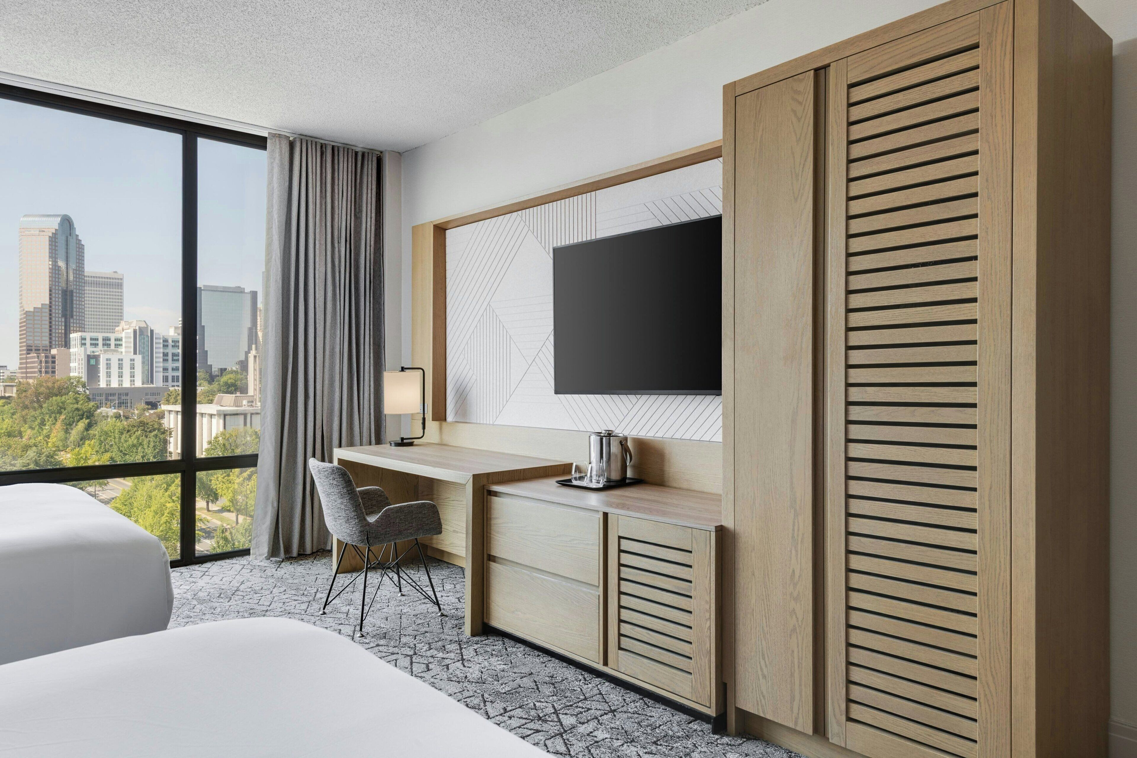 Habitación de hotel con un ventanal grande, una cama, un escritorio con silla, televisor y armario.