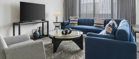A modern living room with a blue sofa, a glass coffee table, a flat-screen TV, and a lamp.