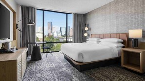 A hotel room with a large bed, a desk, a chair, a TV, and a view of the city. - Sheraton Charlotte Hotel (Charlotte)