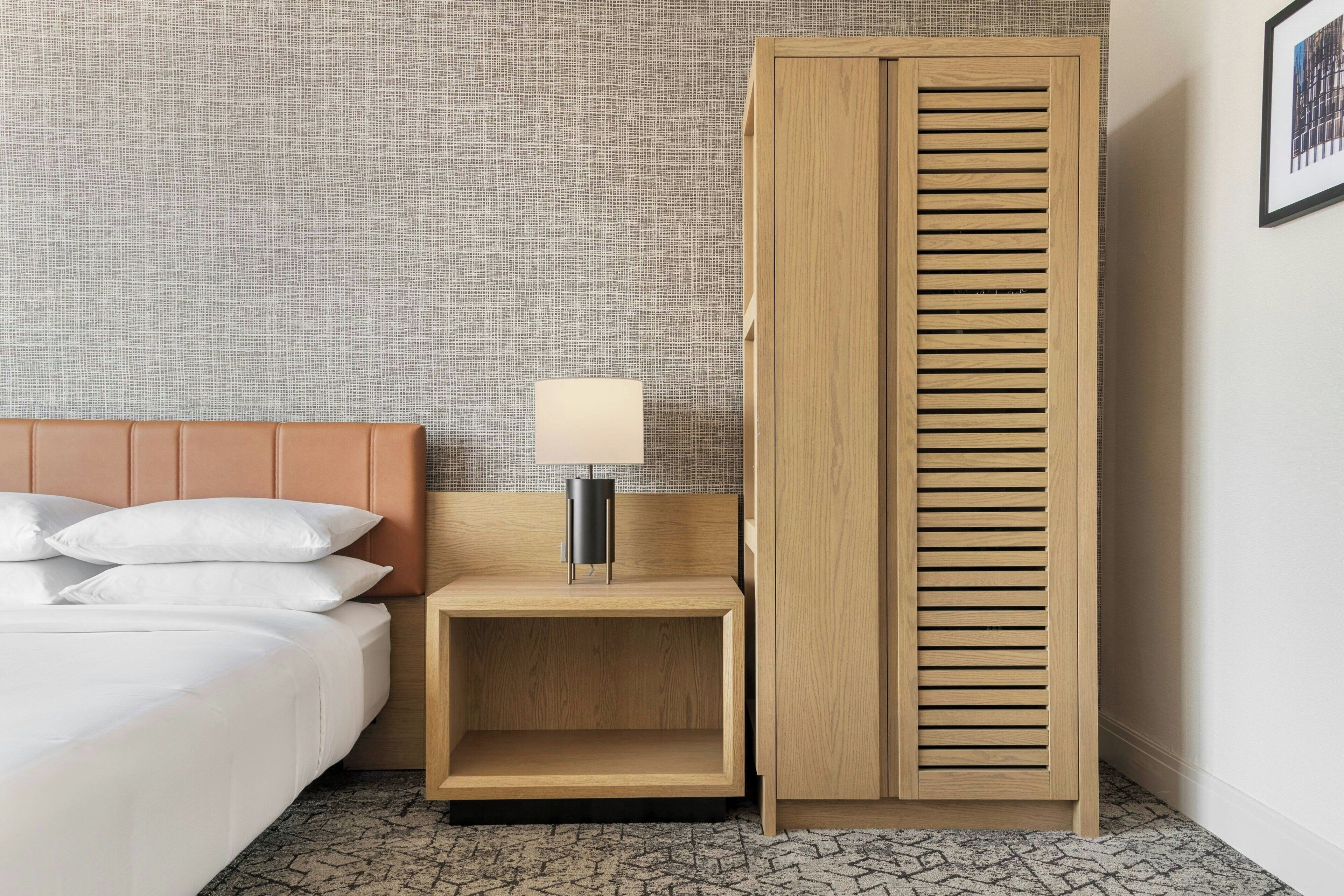 Une chambre d’hôtel avec un lit, une table de chevet avec une lampe, une armoire en bois et un mur à texture.