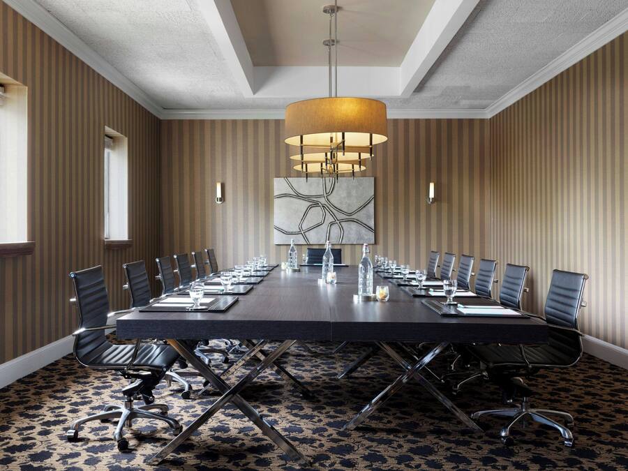 A conference room with a long table, chairs, a chandelier, and a patterned carpet.