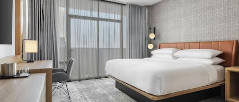 A hotel room with a bed, a desk, a chair, a lamp, and a large window with curtains.