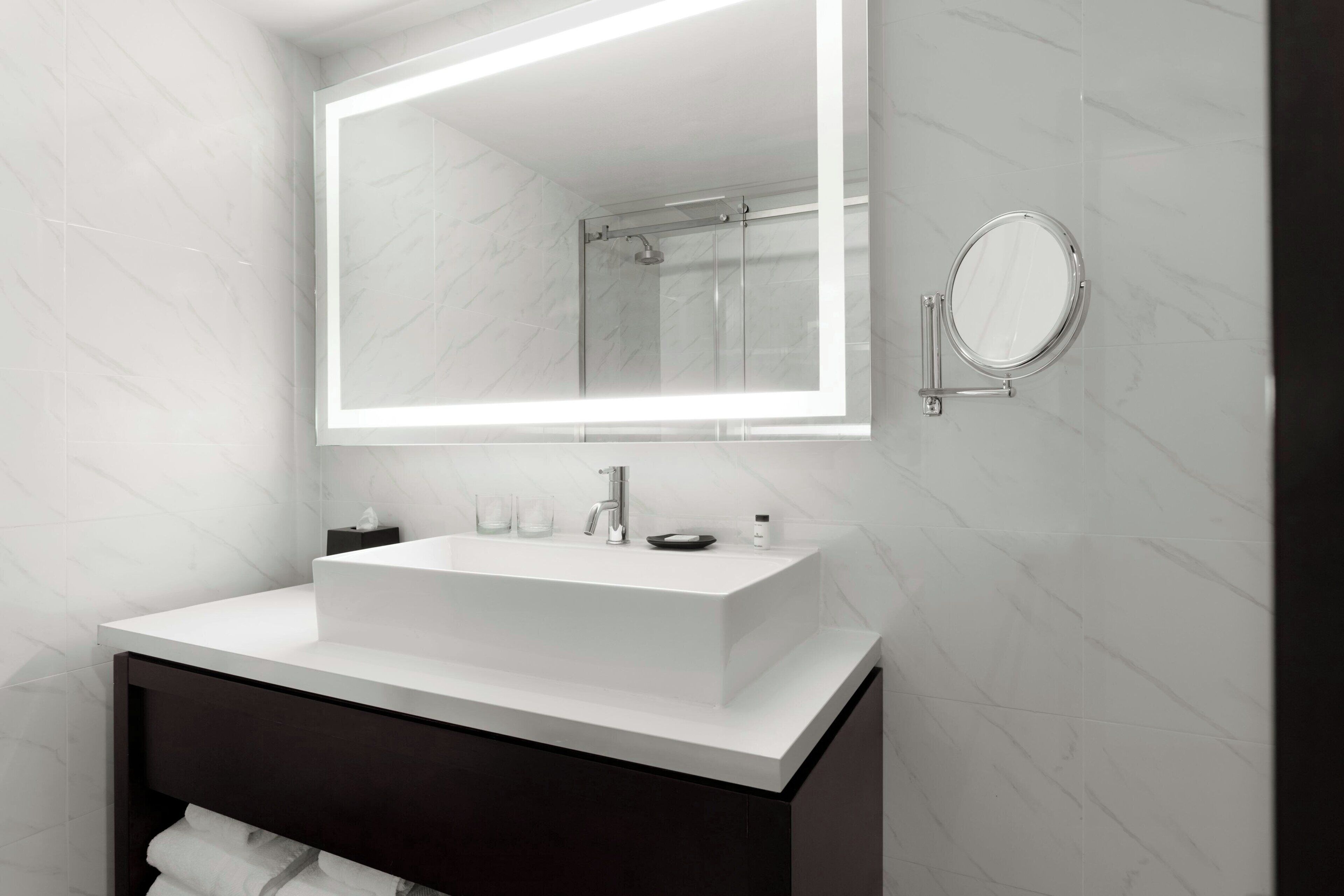 A modern bathroom with a white vanity, a large mirror, and a glass-enclosed shower.