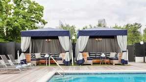 A poolside area with two covered seating areas, each with a canopy and curtains, and a pool with a wooden deck and lounge chairs. - Sheraton Charlotte Hotel (Charlotte)