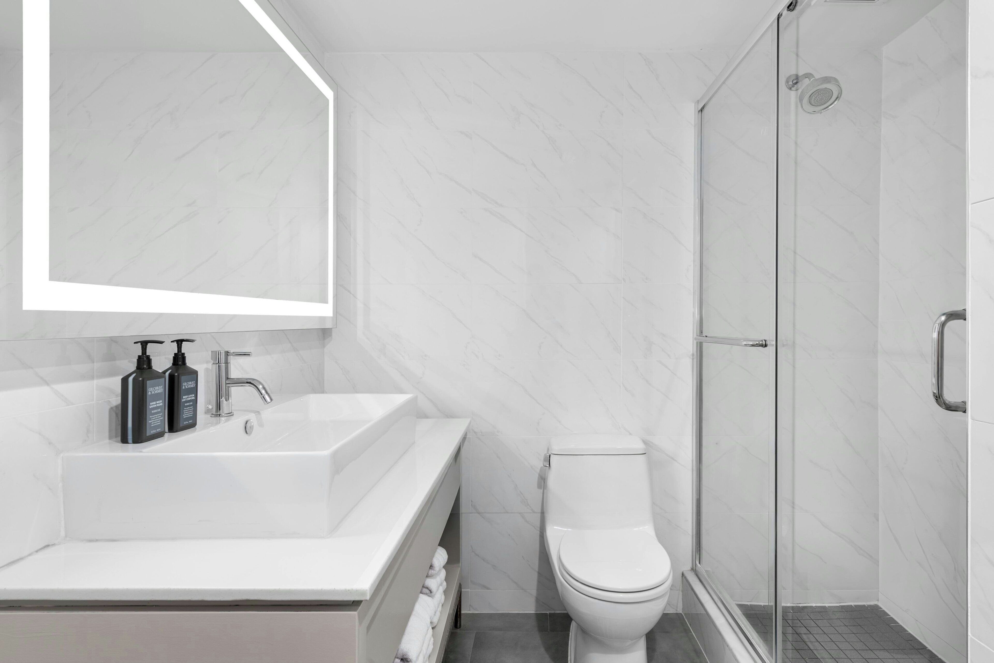Une salle de bain moderne avec un lavabo blanc, des toilettes et une douche à parois de verre.