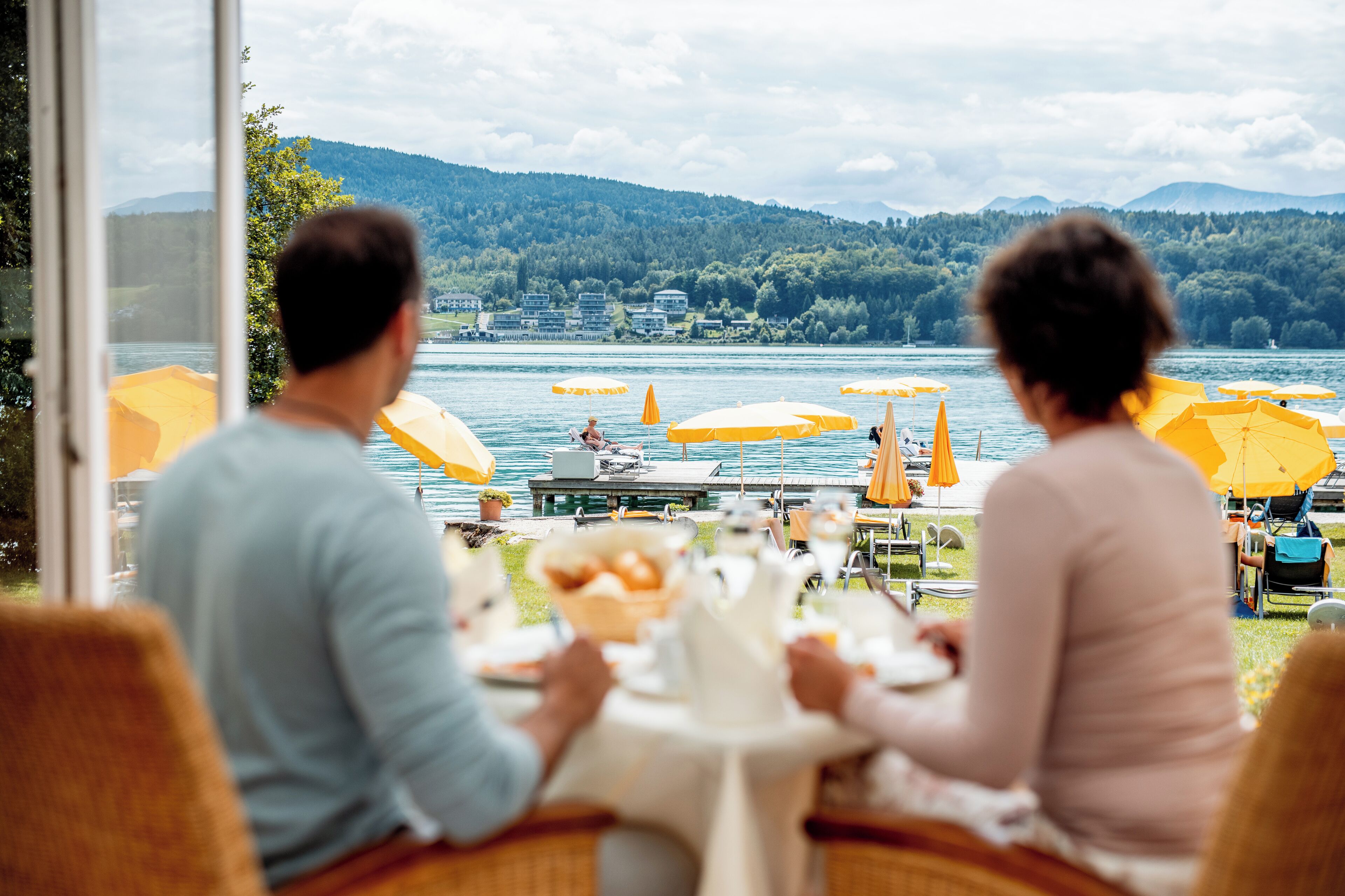 Ein Paar speist an einem Tisch mit Blick auf einen See und Berge.