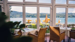 Ein Restaurant mit Terrassensitzung mit Blick auf einen See, ausgestattet mit Korbstühlen und Sonnenschirmen.