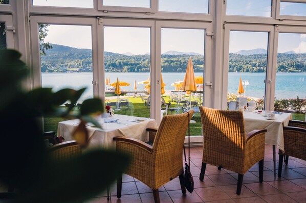A restaurant with outdoor seating overlooking a lake, featuring wicker chairs and umbrellas.