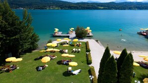 A lakeside resort with sun loungers and umbrellas, a dock, and a clear view of the lake and mountains. - Werzers Seehotel Wallerwirt (Techelsberg am Worther See)
