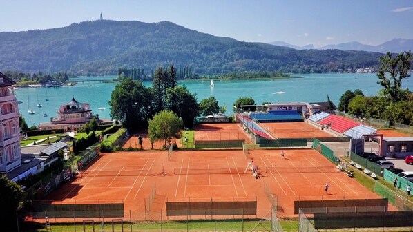 A tennis court with a view of a lake and mountains in the background. - Werzers Seehotel Wallerwirt (Techelsberg am Worther See)