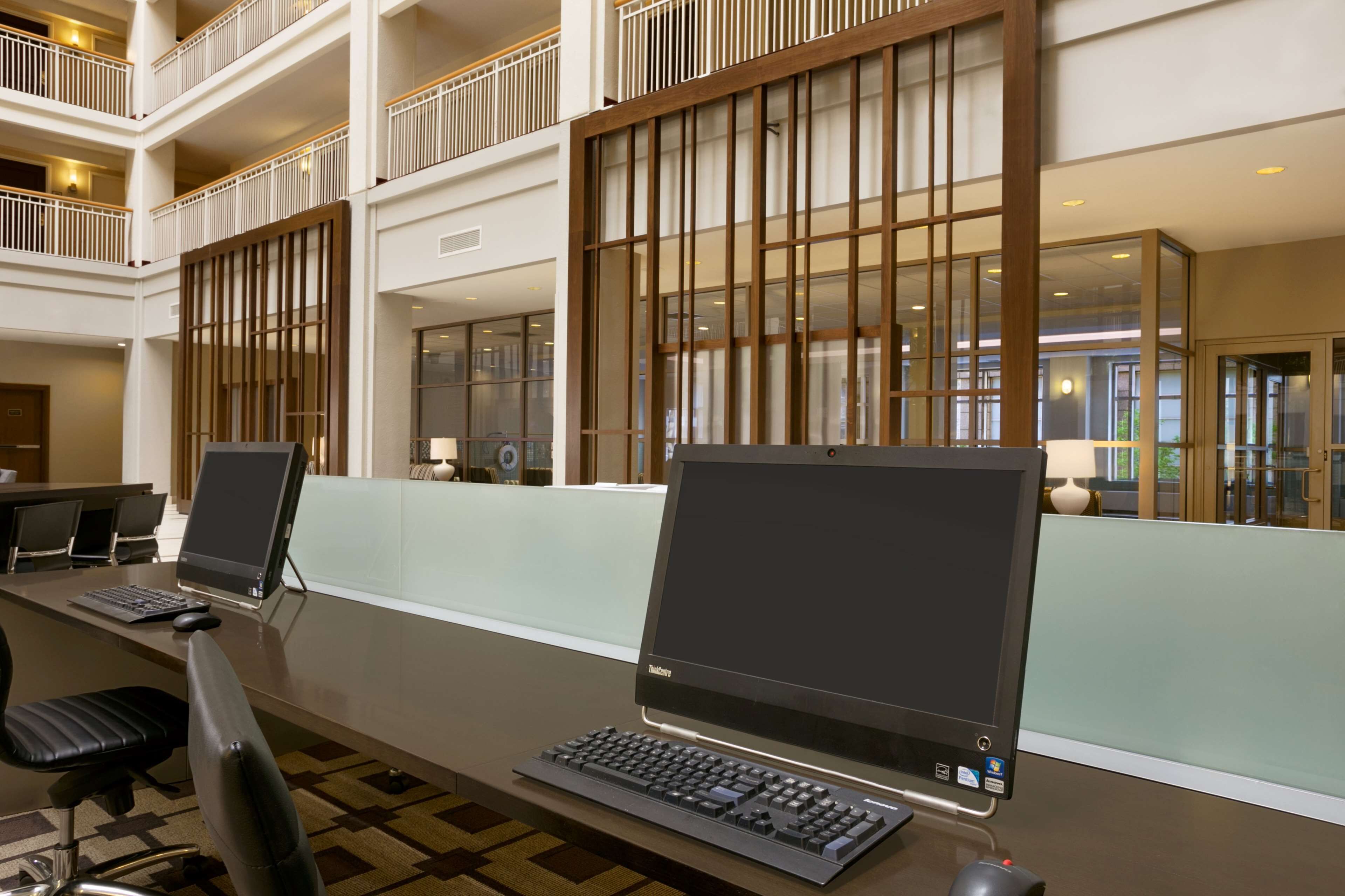 A modern hotel lobby with a long reception desk, two computer stations, and a high ceiling with a balcony.
