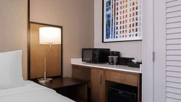 Habitación de hotel con cama, escritorio con lámpara, cafetera, microondas y refrigerador.