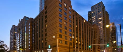 A multi-story hotel with a prominent 'Embassy Suites' sign, located at a city intersection with traffic lights and other buildings in the background.