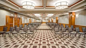 A conference room with rows of chairs, a patterned carpet, wooden paneling, and exit signs.