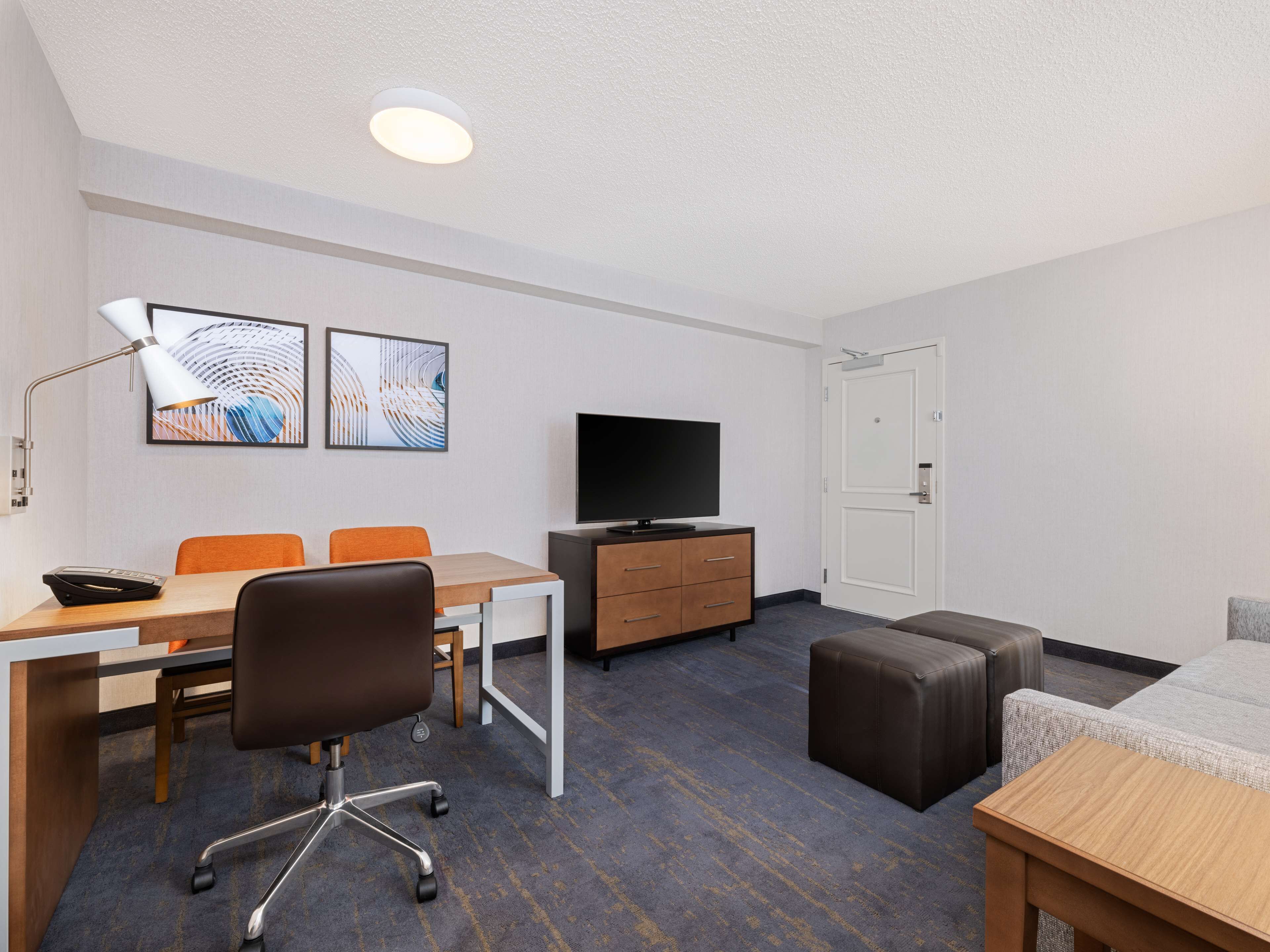 A hotel room with a desk, two chairs, a television, a cabinet, a door, and a small couch.