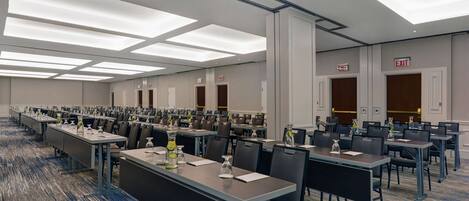 Uma sala de conferências ampla com várias mesas e cadeiras, equipada com porta-nomes e garrafas de água.