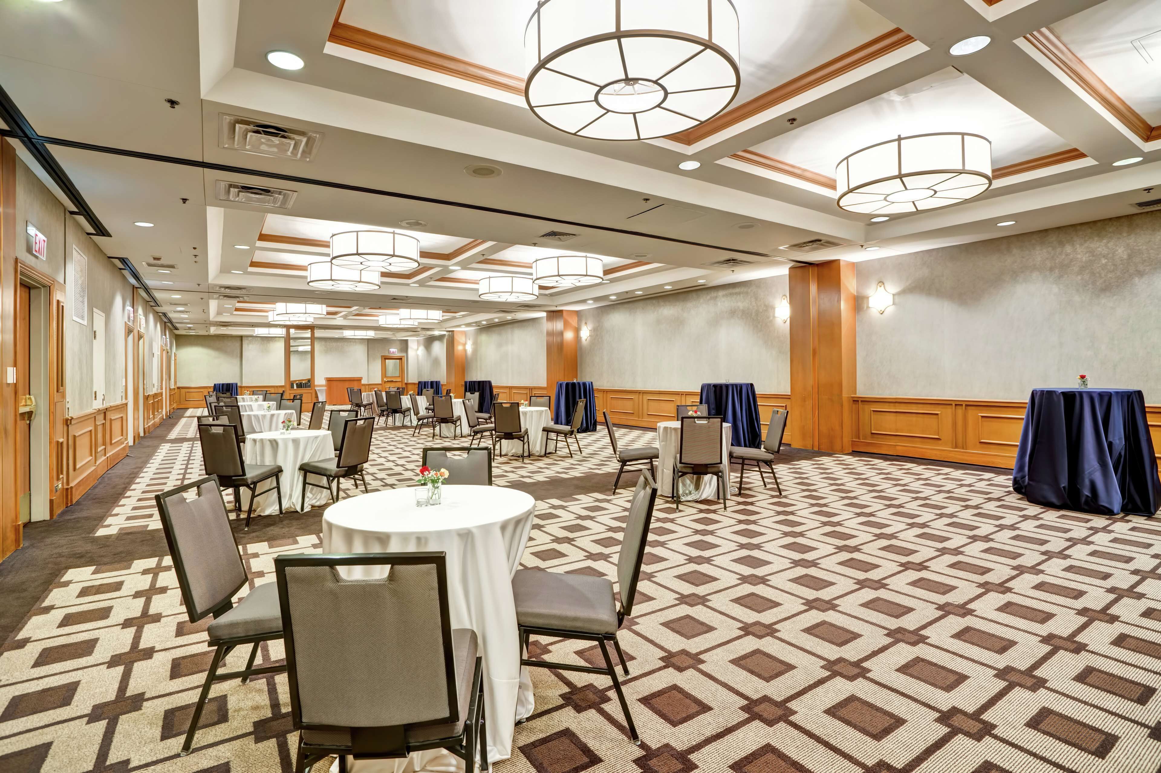 A spacious conference room with round tables, chairs, and a patterned carpet.