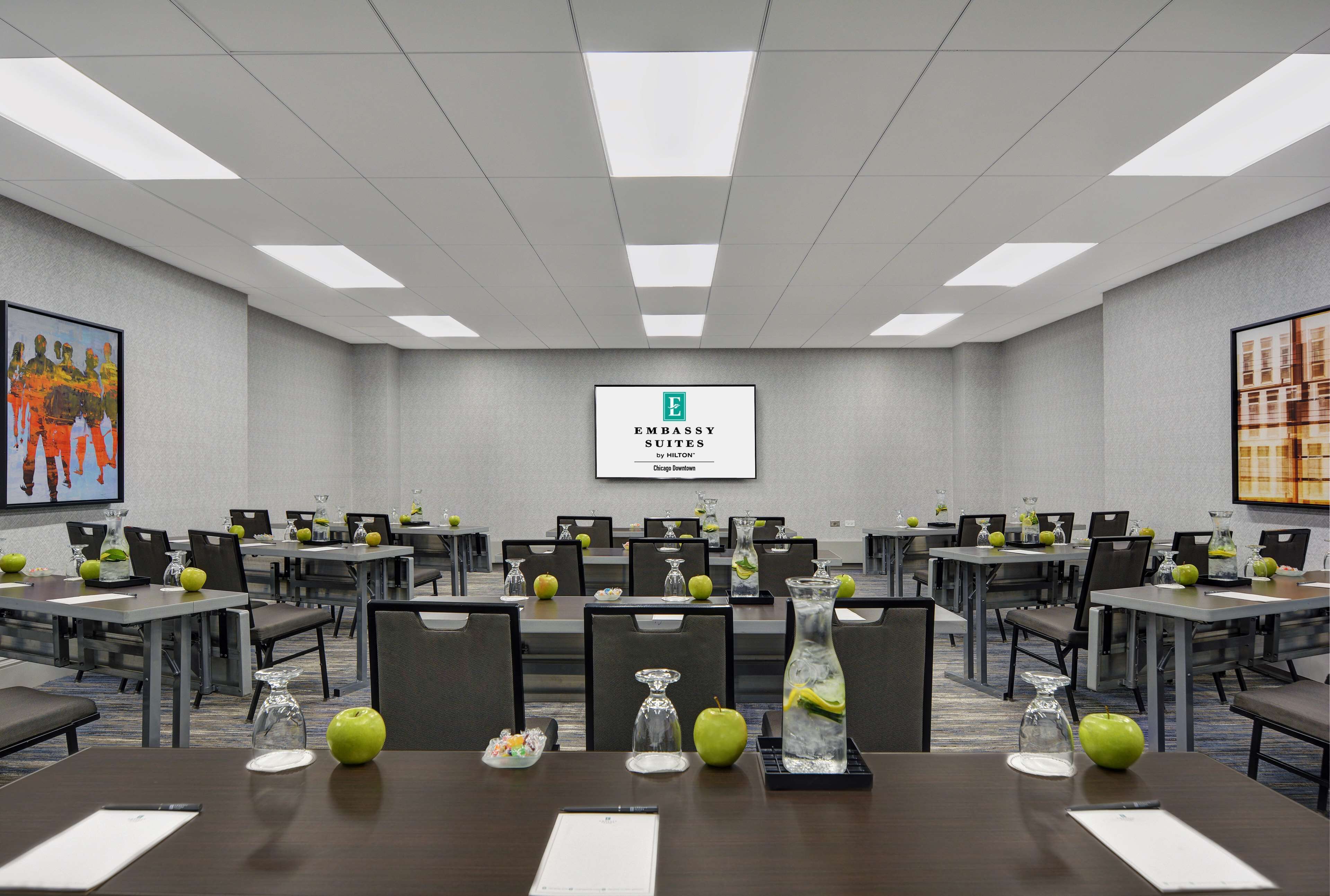 A conference room with tables, chairs, and a large screen displaying "Embassy Suites by Hilton Chicago Downtown".