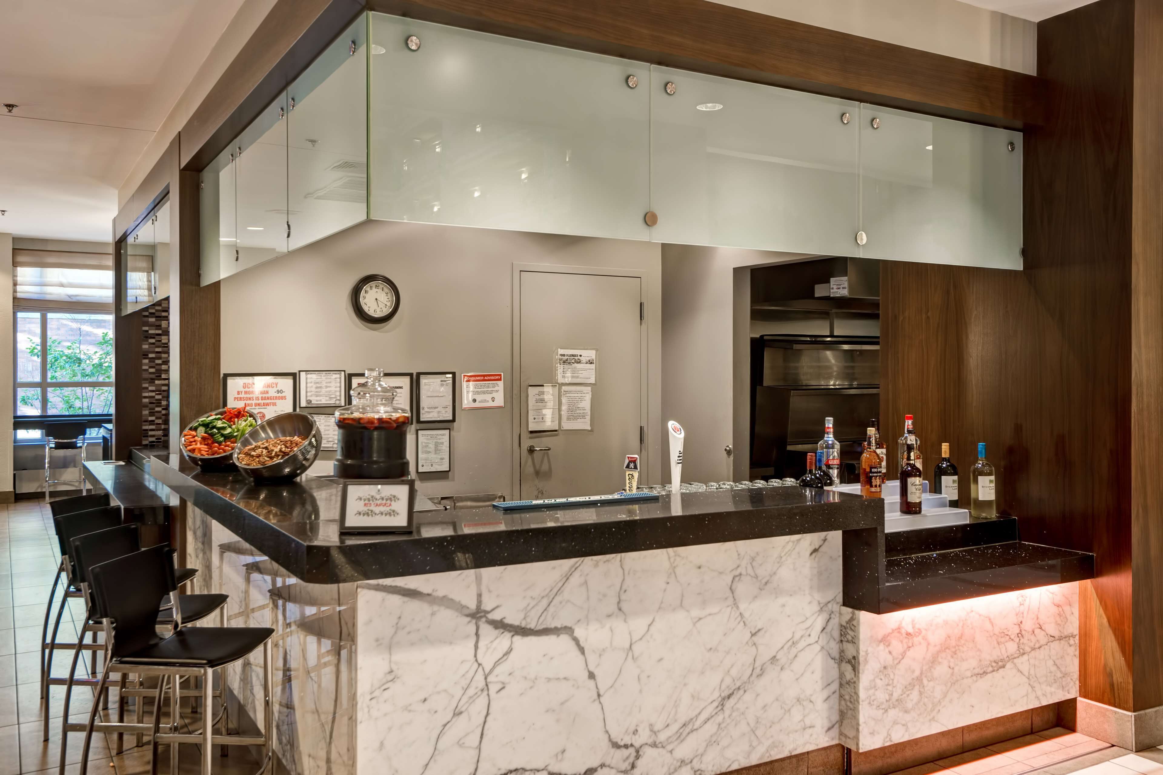 A modern kitchen with a marble countertop, glass cabinets, and a bar area with stools.