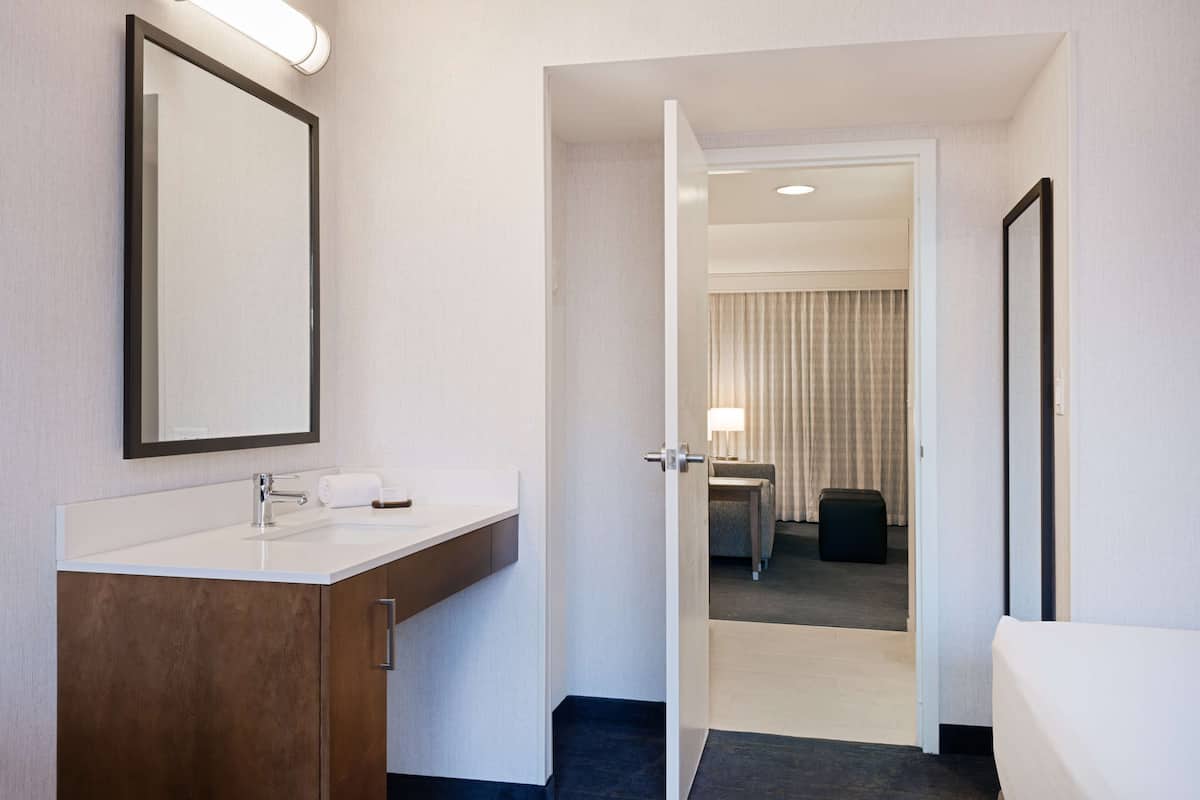 A hotel bathroom with a large mirror, a sink, and a wooden cabinet.