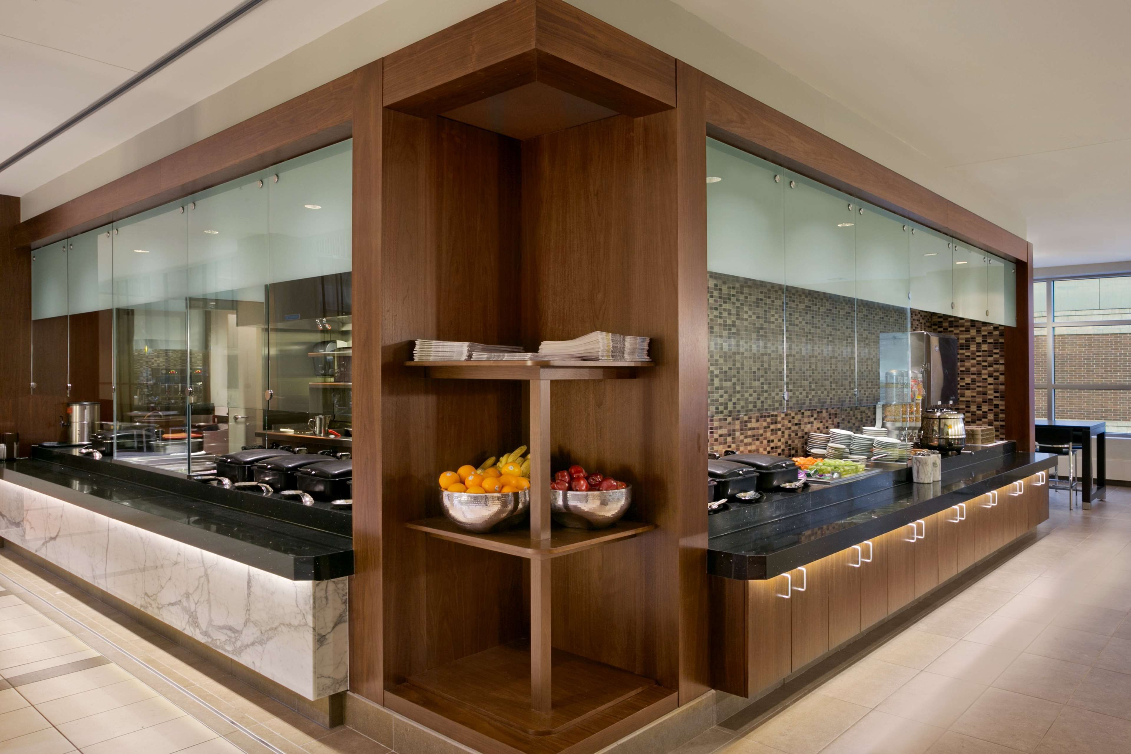 A modern kitchen with a marble countertop, wooden cabinetry, and a central island with fruit bowls.