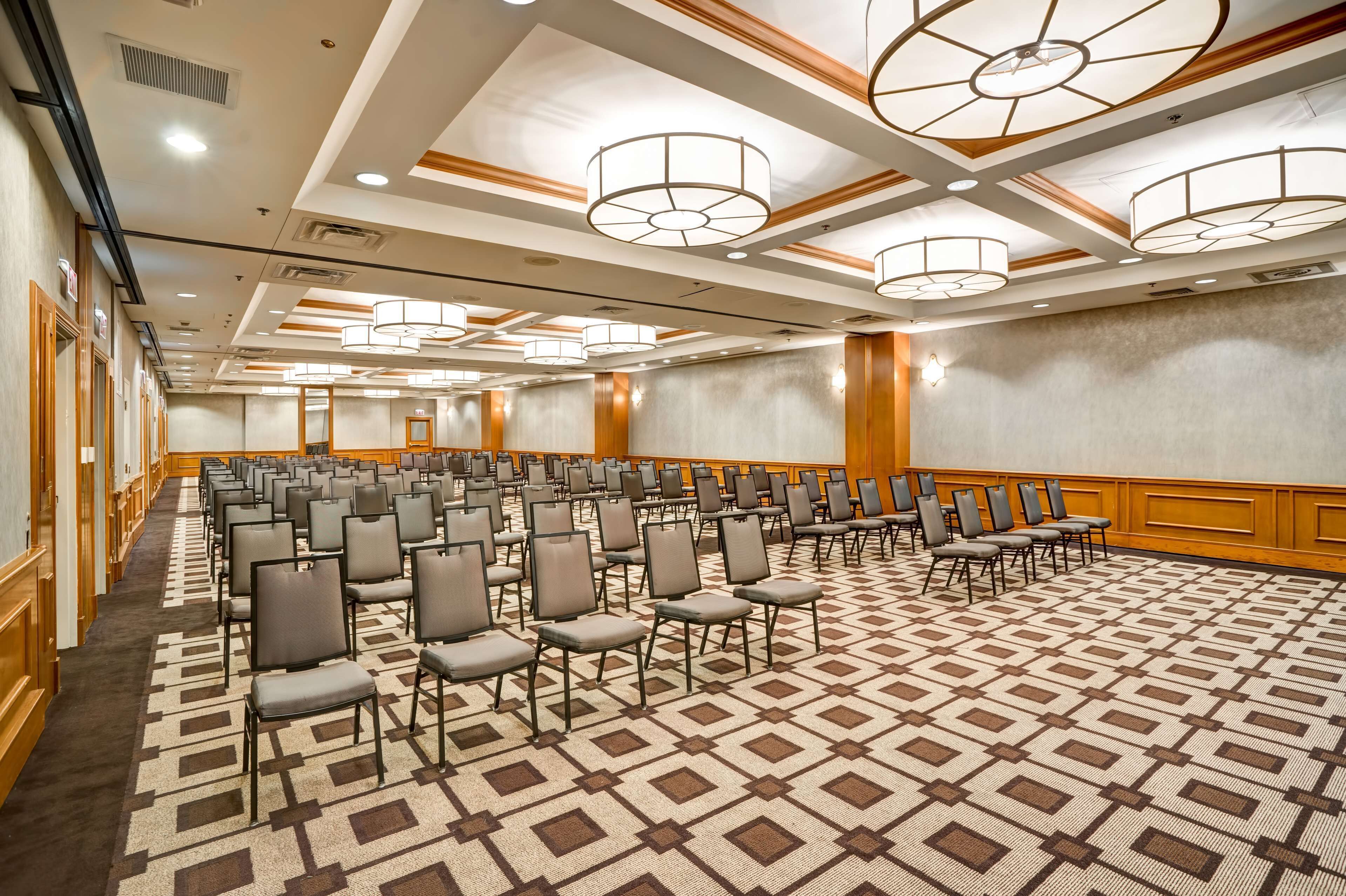 A conference room with rows of chairs, a patterned carpet, and ceiling lights.