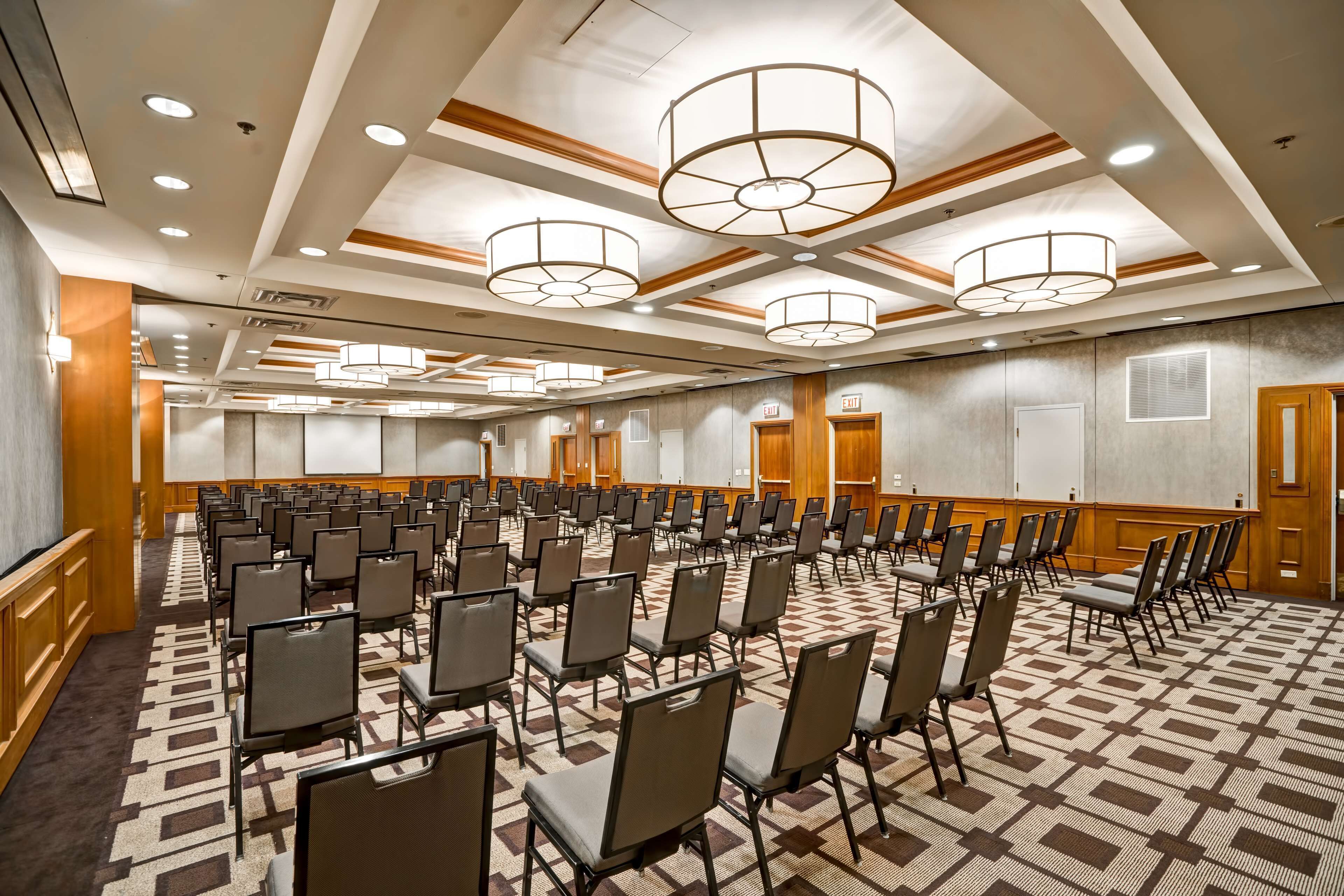A conference room with rows of chairs, wooden paneling, and recessed lighting.