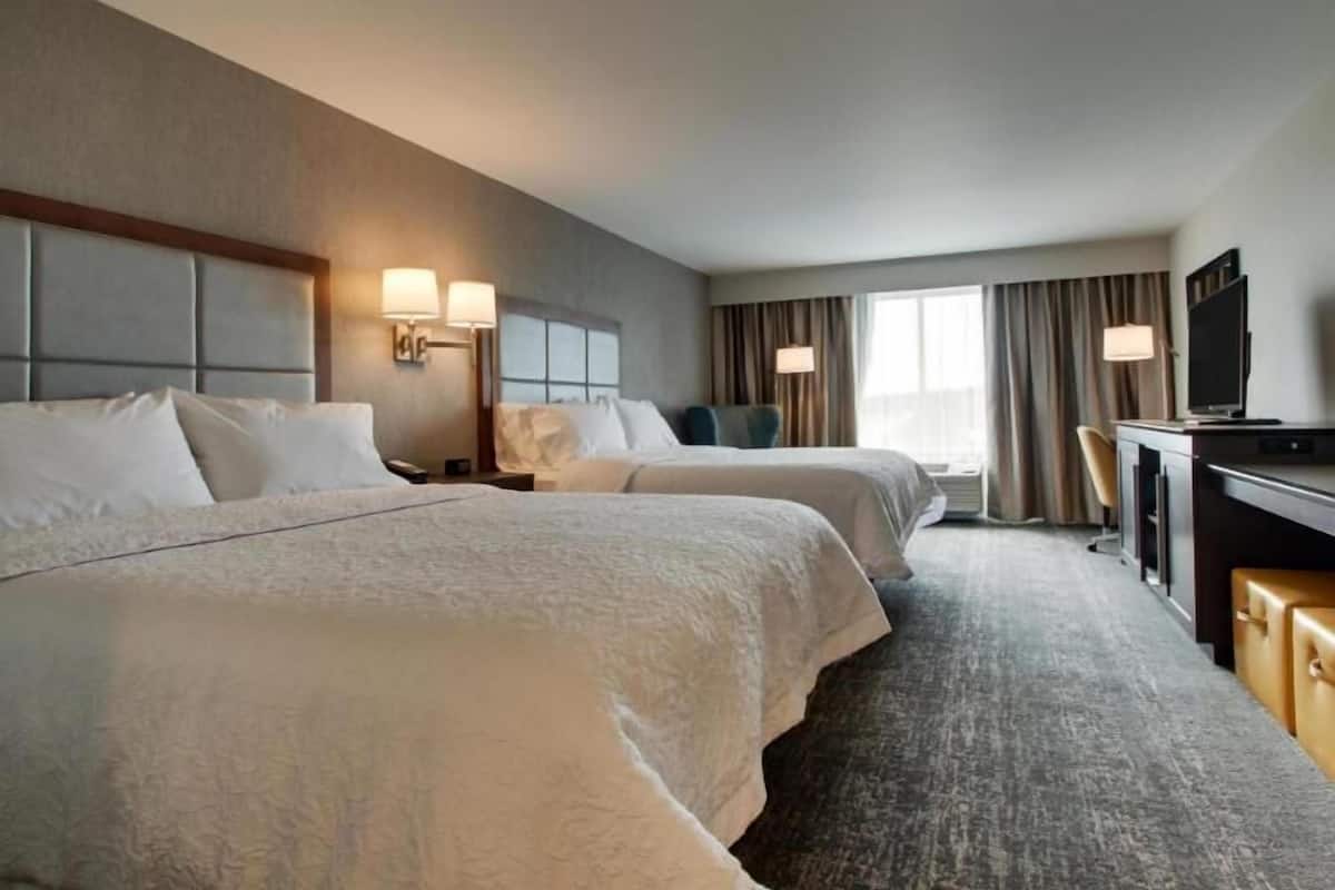 Habitación de hotel con dos camas, un escritorio con televisor y una ventana con cortinas.