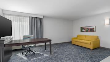 A hotel room with a desk, chair, sofa, and a painting on the wall.