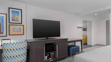 A hotel room with a flat-screen TV, a desk, a microwave, a blue chair, and a bed.
